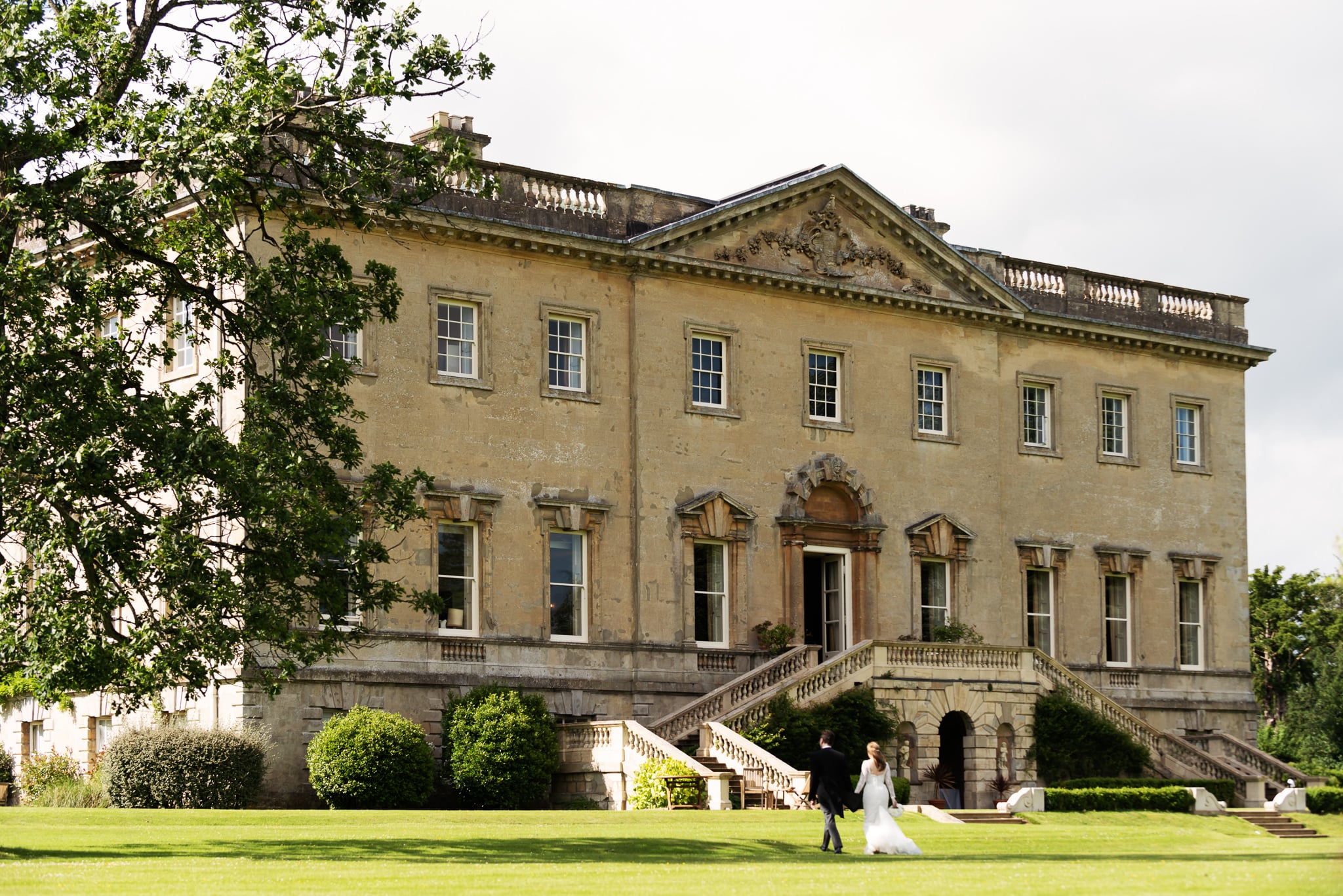 A wide shot of Kirtlington Park with the bride and groom walking towards it.