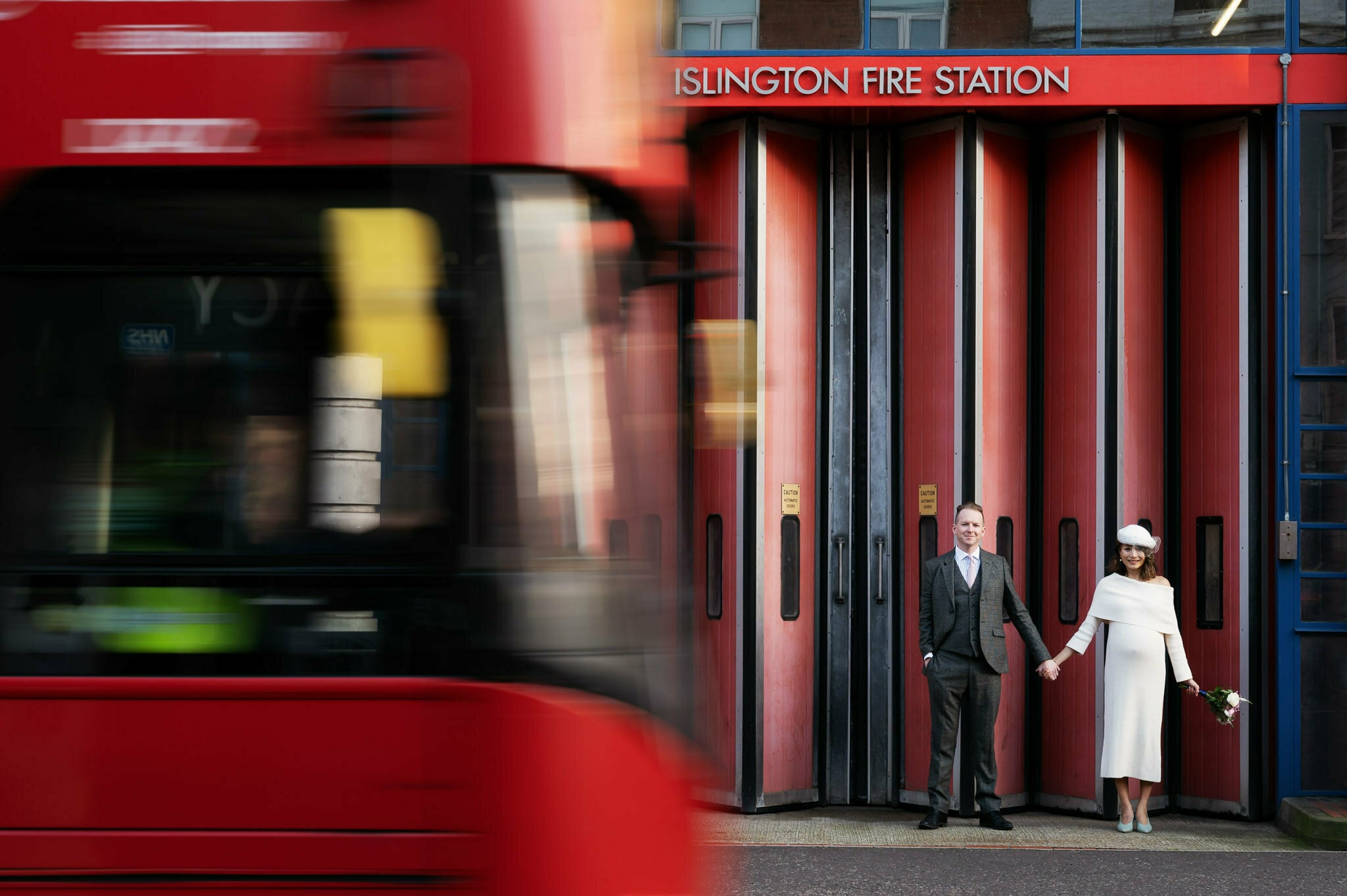 Modern portrait of bride and groom in front of Islington Town Hall as a London bus passes