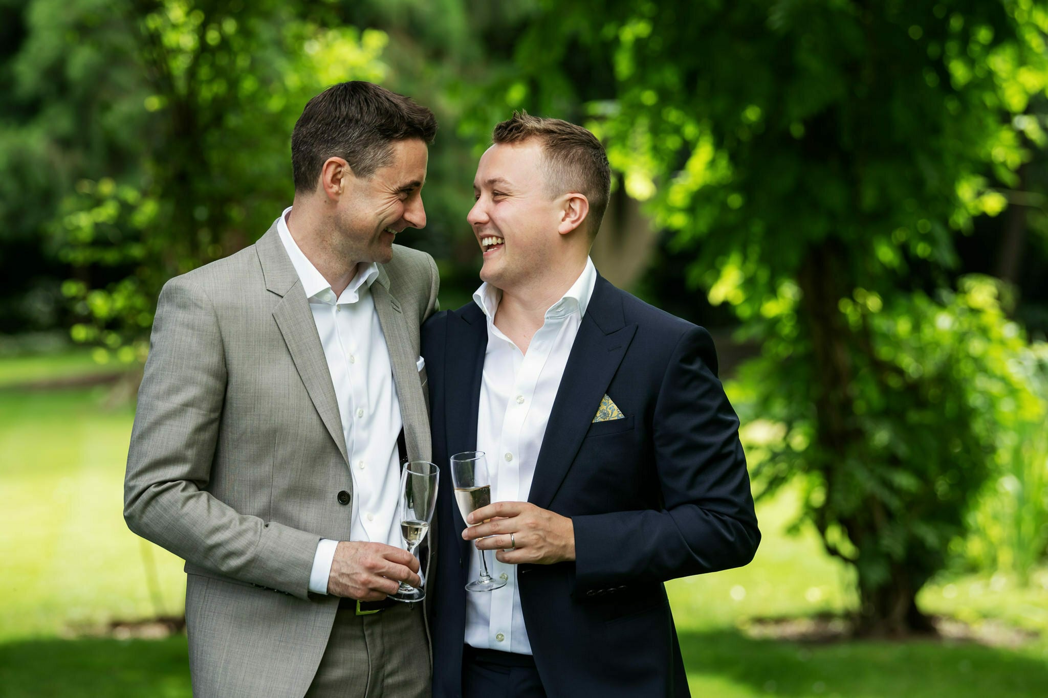 Two grooms laughing together in the gardens at St Michael’s Manor wedding