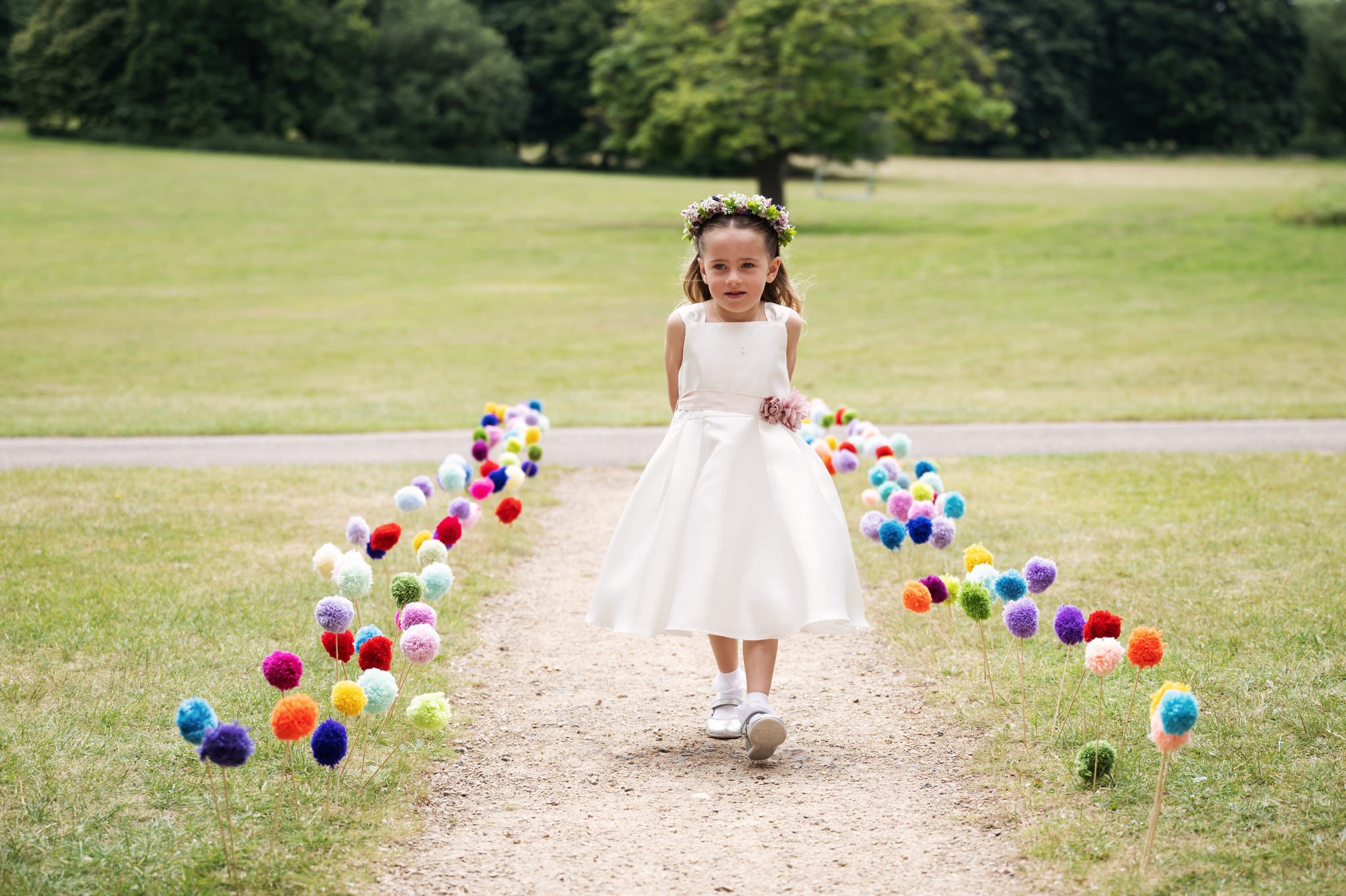 A flower girl walks up the aisle at the beginning of an outdoor wedding ceremony at Hitchin Priory.