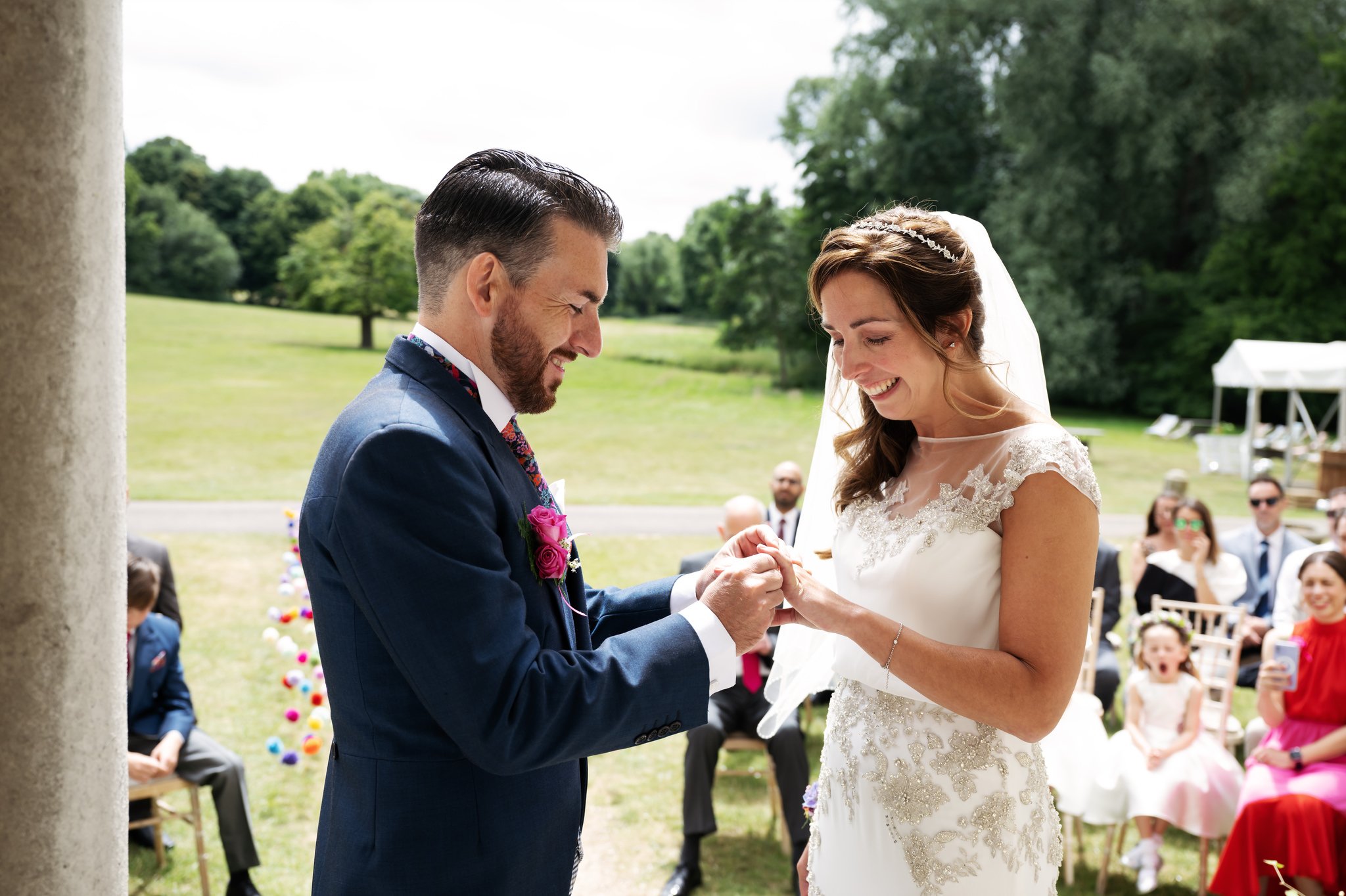 The bride and groom exchange wedding rings during the outdoor wedding ceremony at Hitchin Priory.