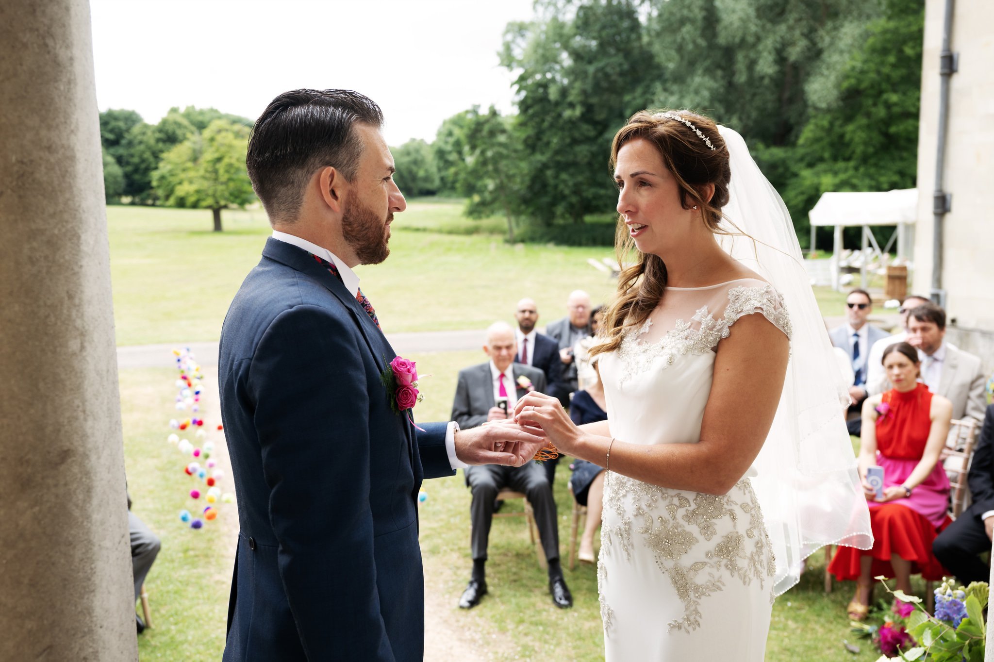 The bride and groom exchange wedding rings during the outdoor wedding ceremony at Hitchin Priory.