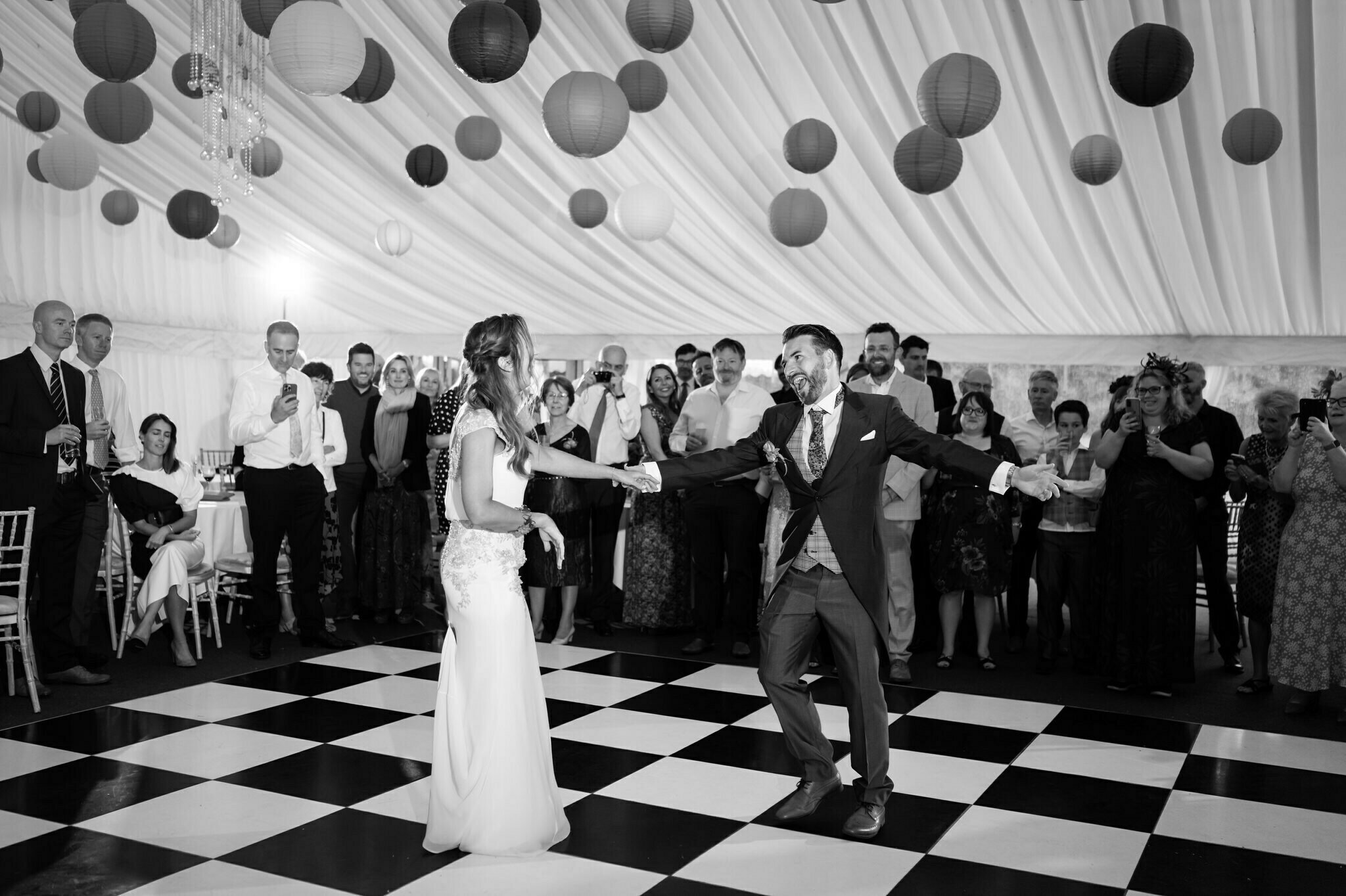 The bride and groom first dance at Hitchin Priory wedding they are dancing in a marquee with a black and white chequerboard dance floor.