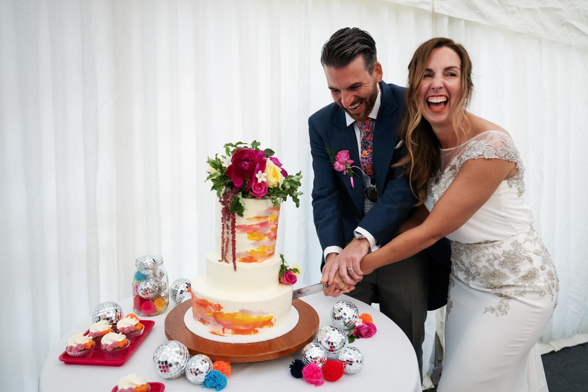 The bride and groom burst into laughter while cutting the wedding cake at a Hitchin Priory wedding.