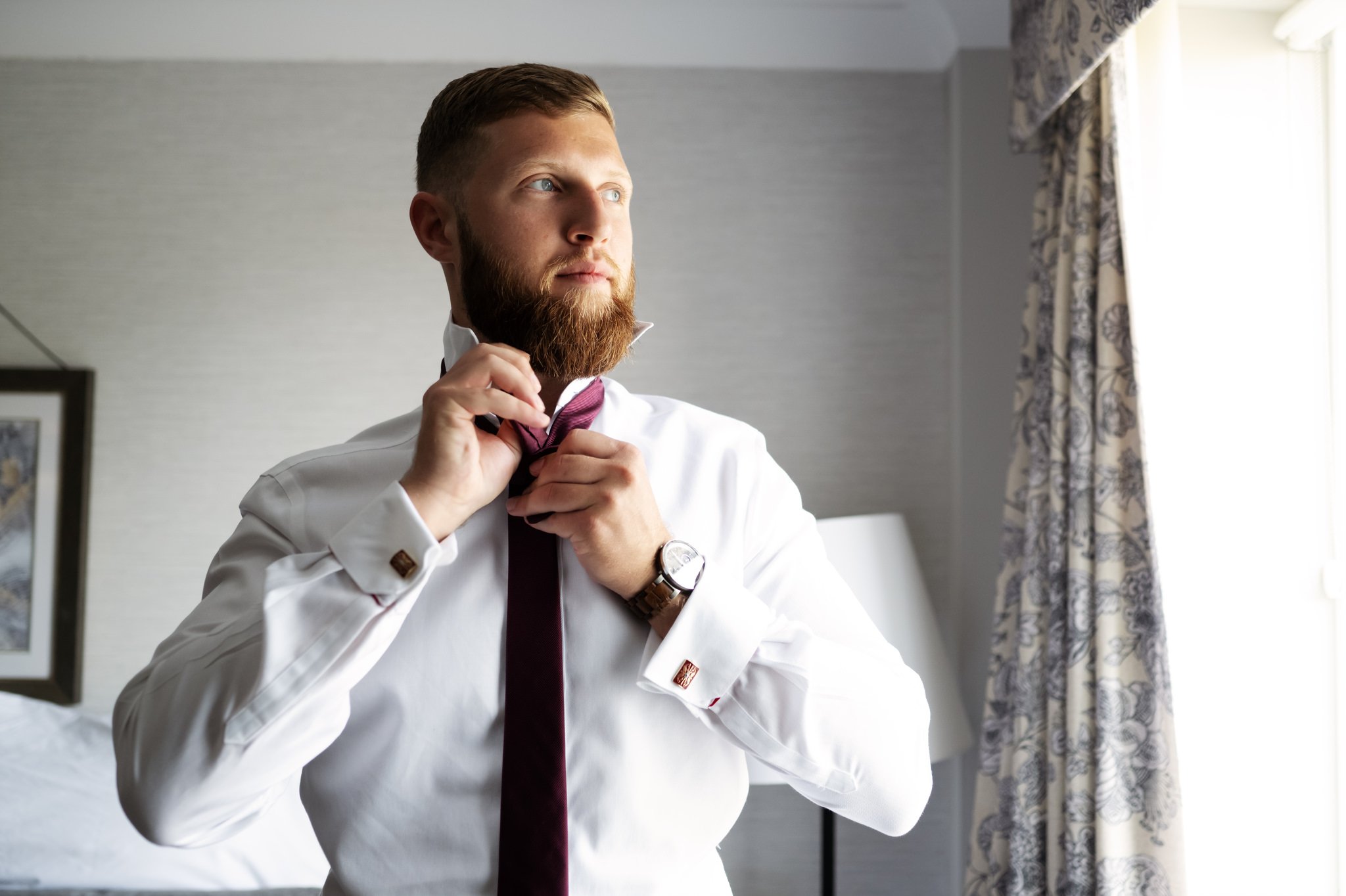 The groom does up his tie at Horwood House.