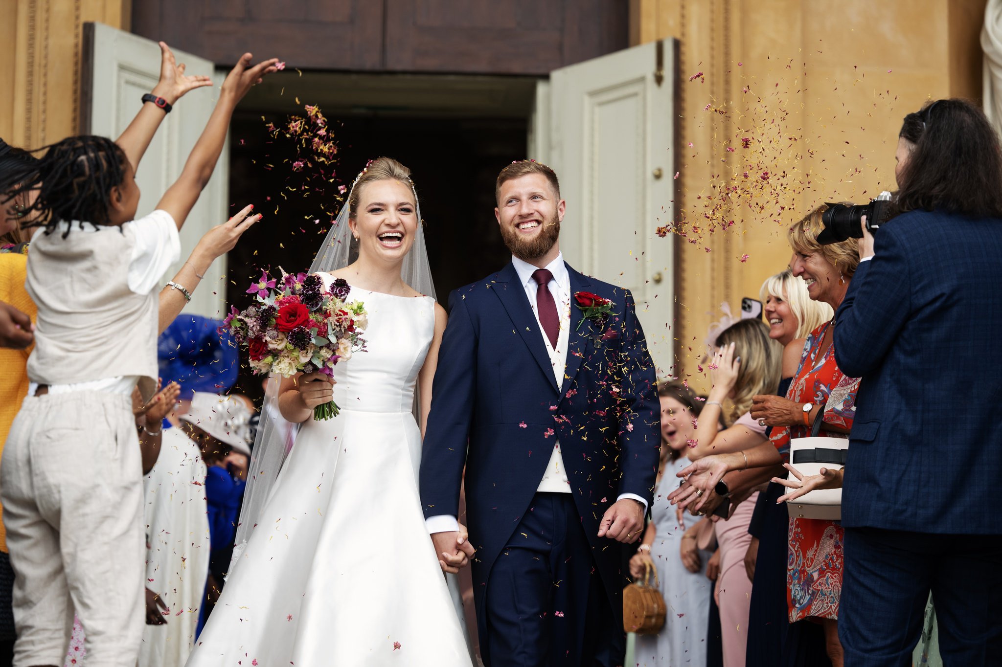 The bride and groom have confetti thrown over them at the end of their wedding ceremony at Stowe House.