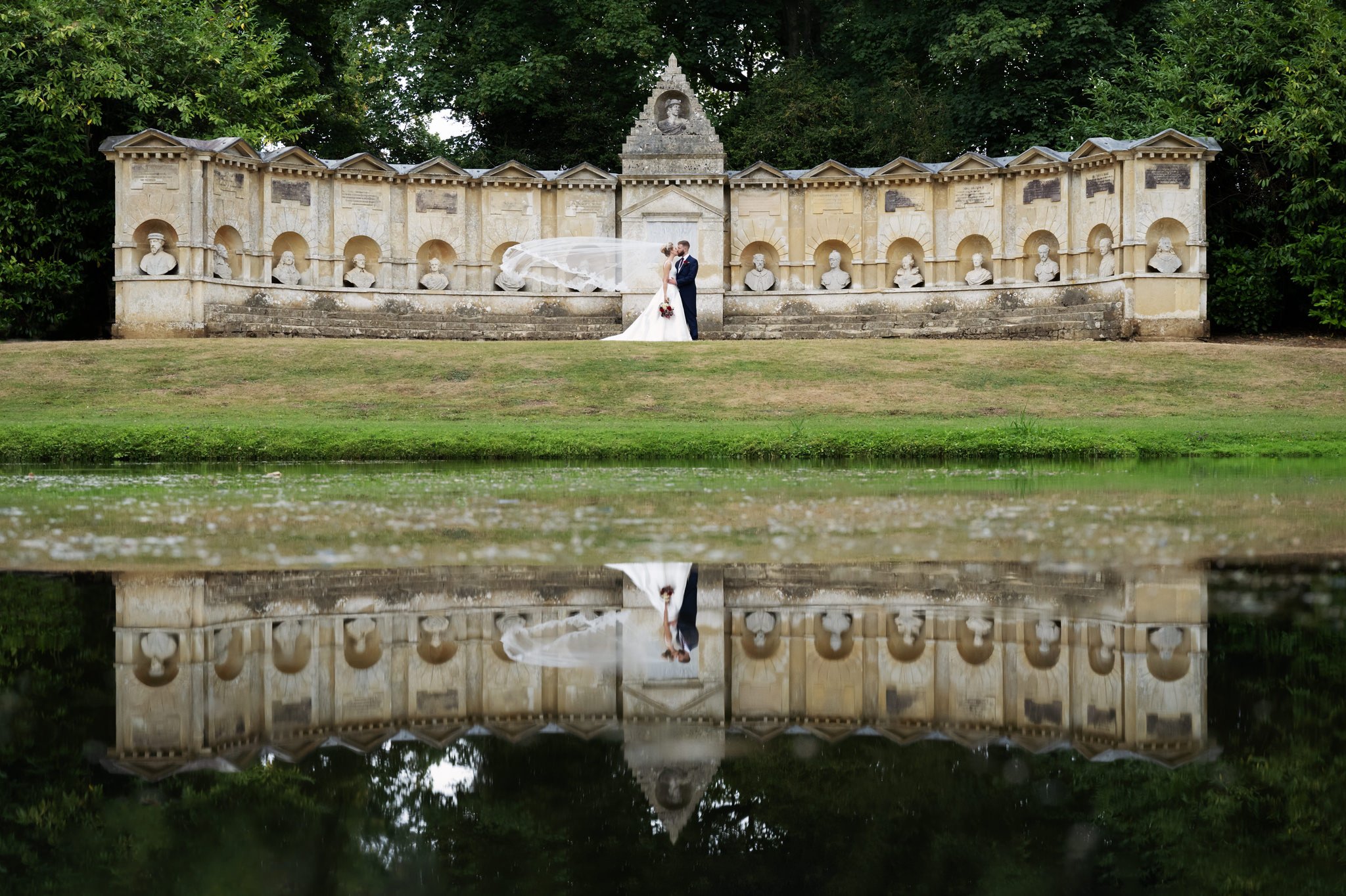 A reflection shot of the bride and groom kissing in front of the Temple of British Worthies at Stowe House. Stowe wedding photographer.