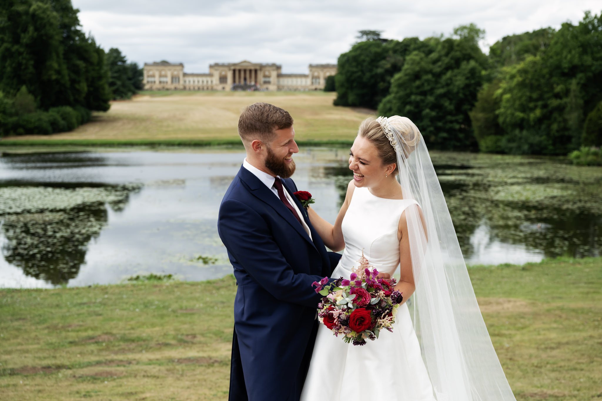 A portrait of the bride and groom laughing with Stowe House in the background.