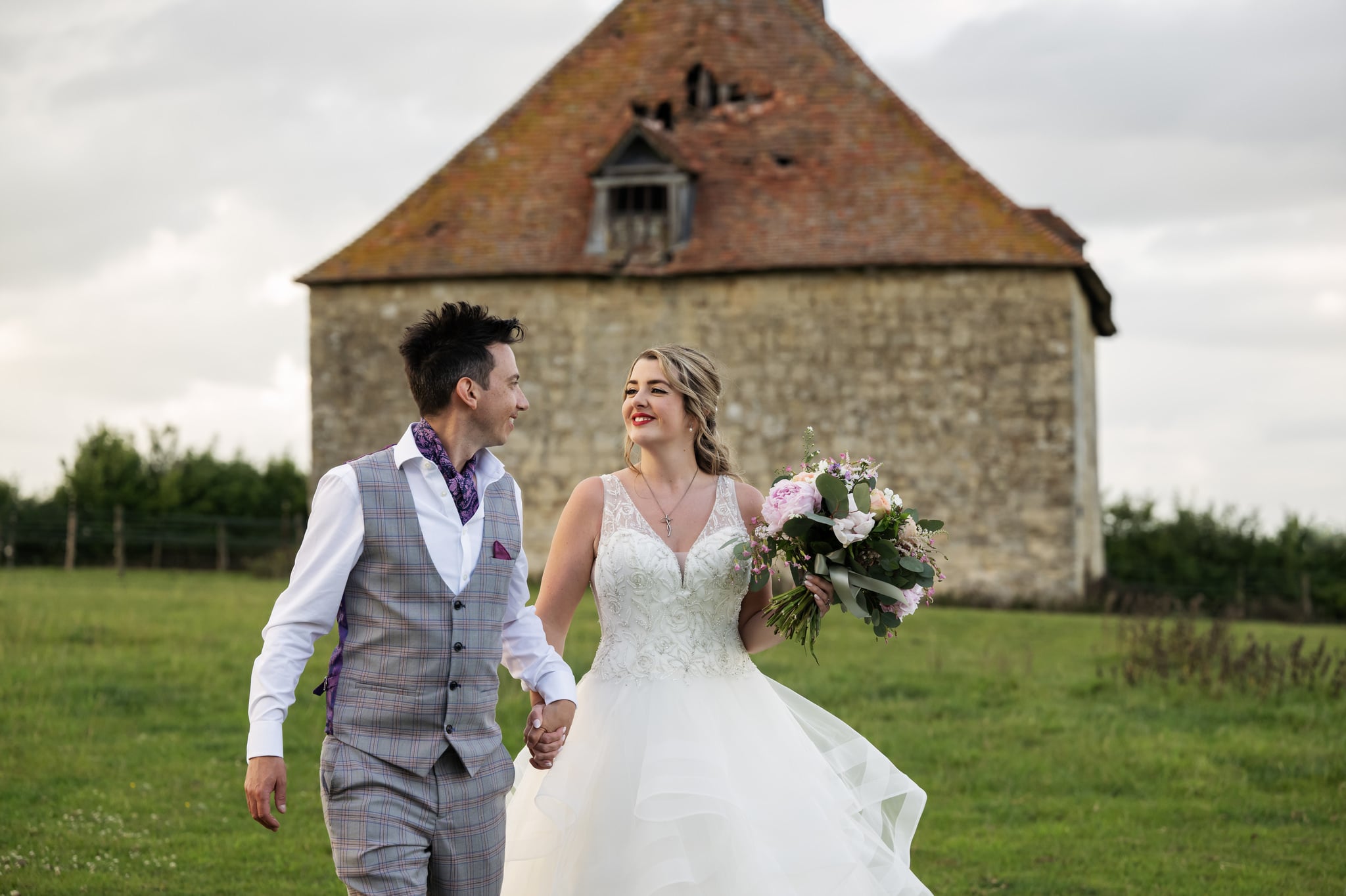 A portrait of the bride and groom walking in front of the dovecote at Notley Tythe Barn wedding.