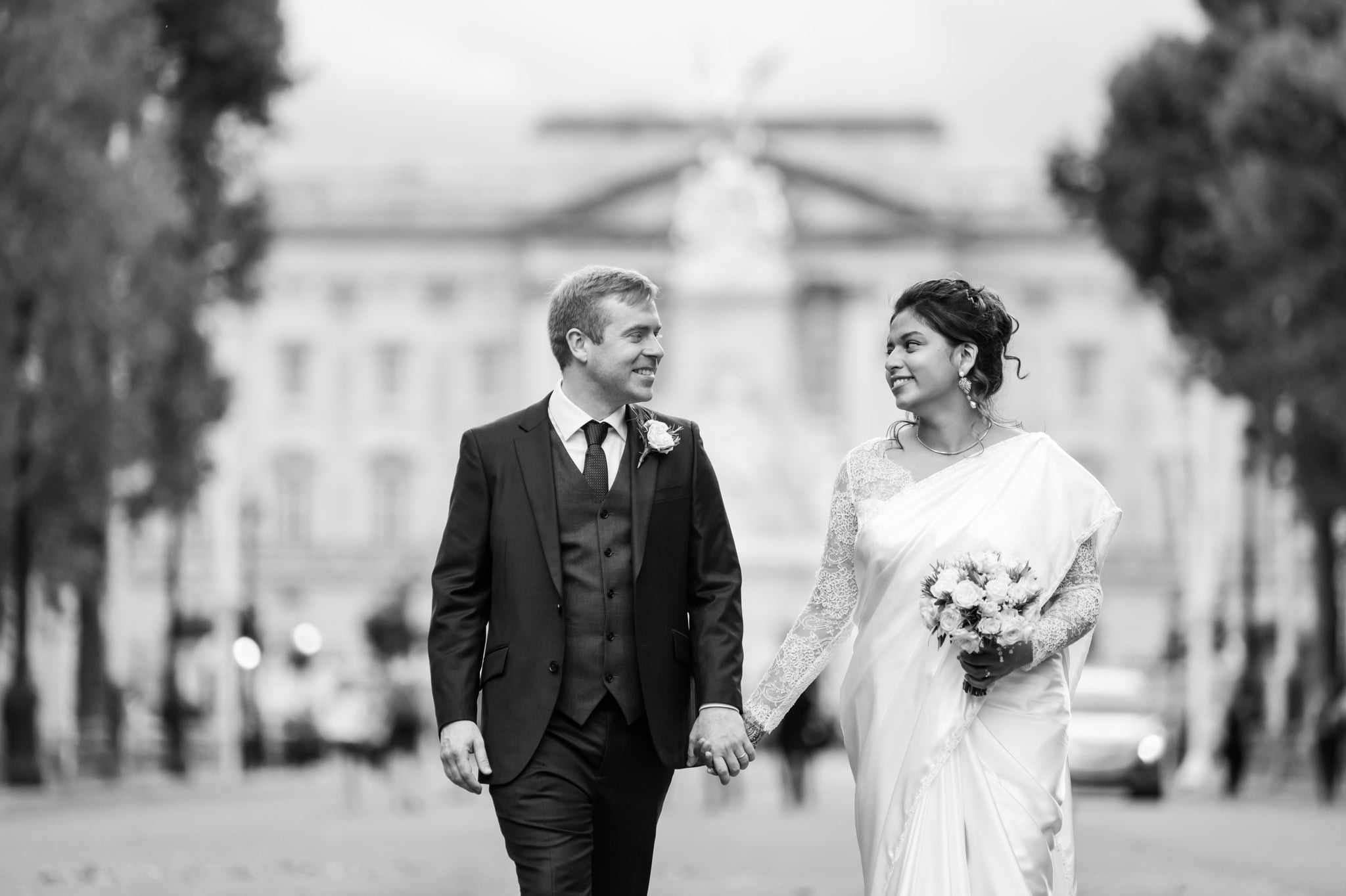 A relaxed portrait of the bride and groom walking hand in hand down the Mall with Buckingham Palace in the background. London wedding photography.