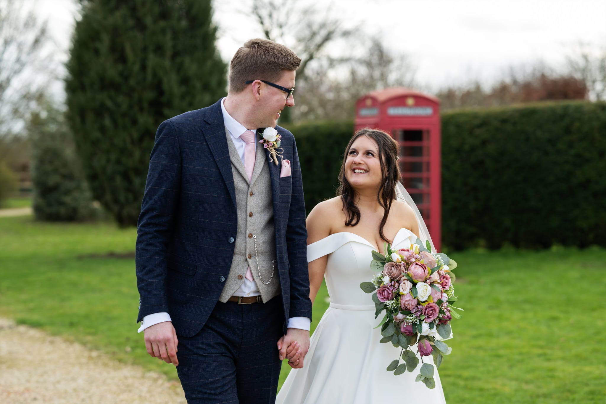 A bride and groom captured by the Huntsmill Farm Wedding Photographer, walking in front of a telephone booth.