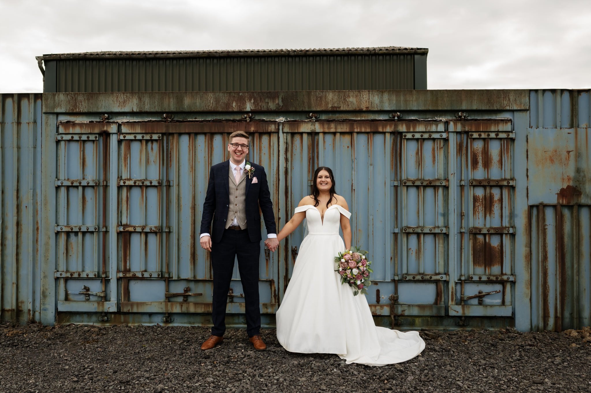 A relaxed portrait bride and groom in front of metal containers at Huntsmill Farm