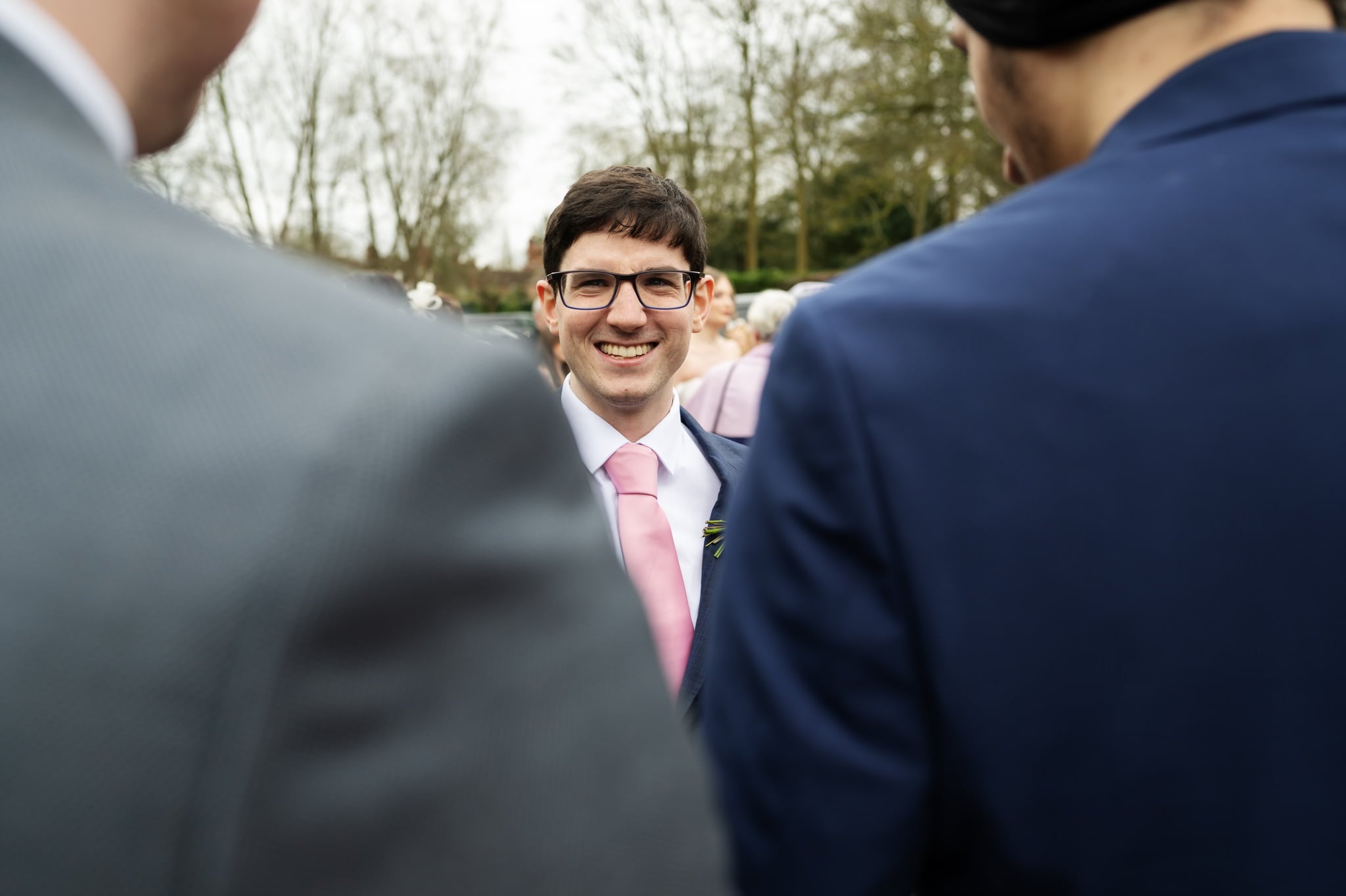 A man in a suit and tie smiles as the Lillibrooke Manor Wedding Photographer captures the moment.