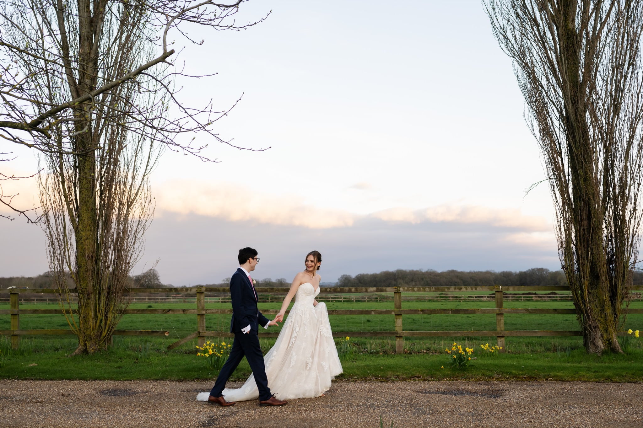 A couple strolling through a field on their wedding day, captured by a Lillibrooke Manor Wedding Photographer.