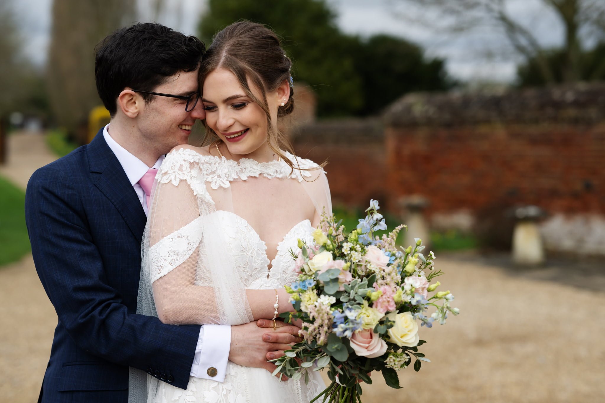 A bride and groom hugging in front of a brick wall, captured by the Lillibrooke Manor Wedding Photographer.
