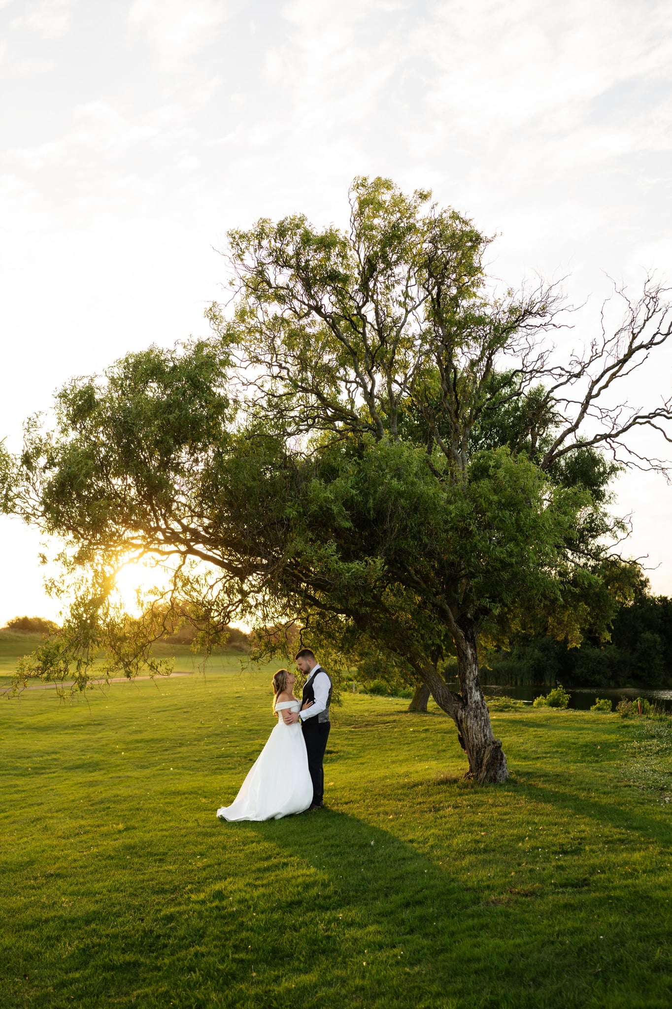 A bride and groom standing under a tree at sunset.