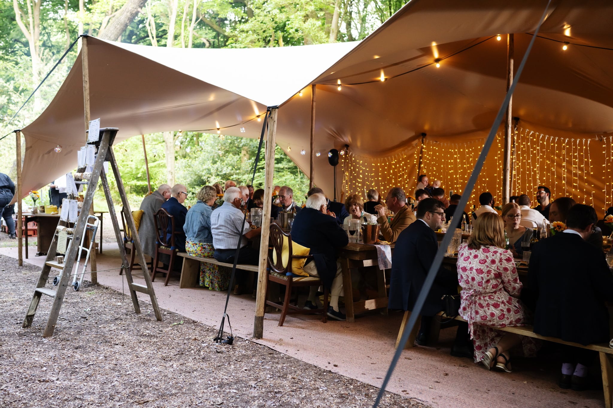 A group of people sitting at tables in a tent in a wooded area.