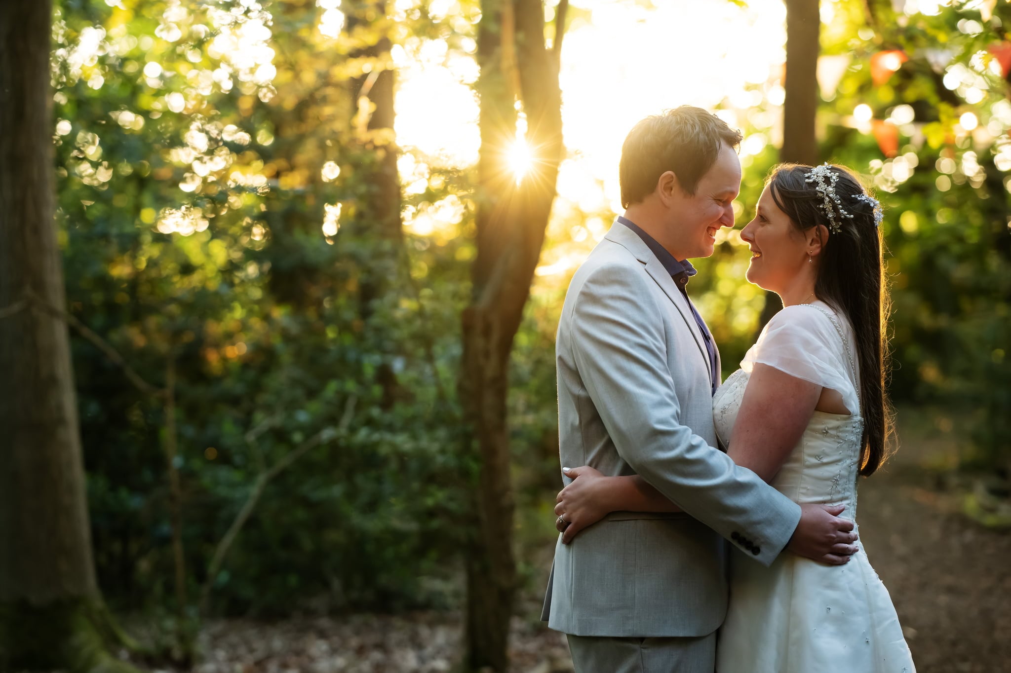 A bride and groom embrace in the woods at sunset.