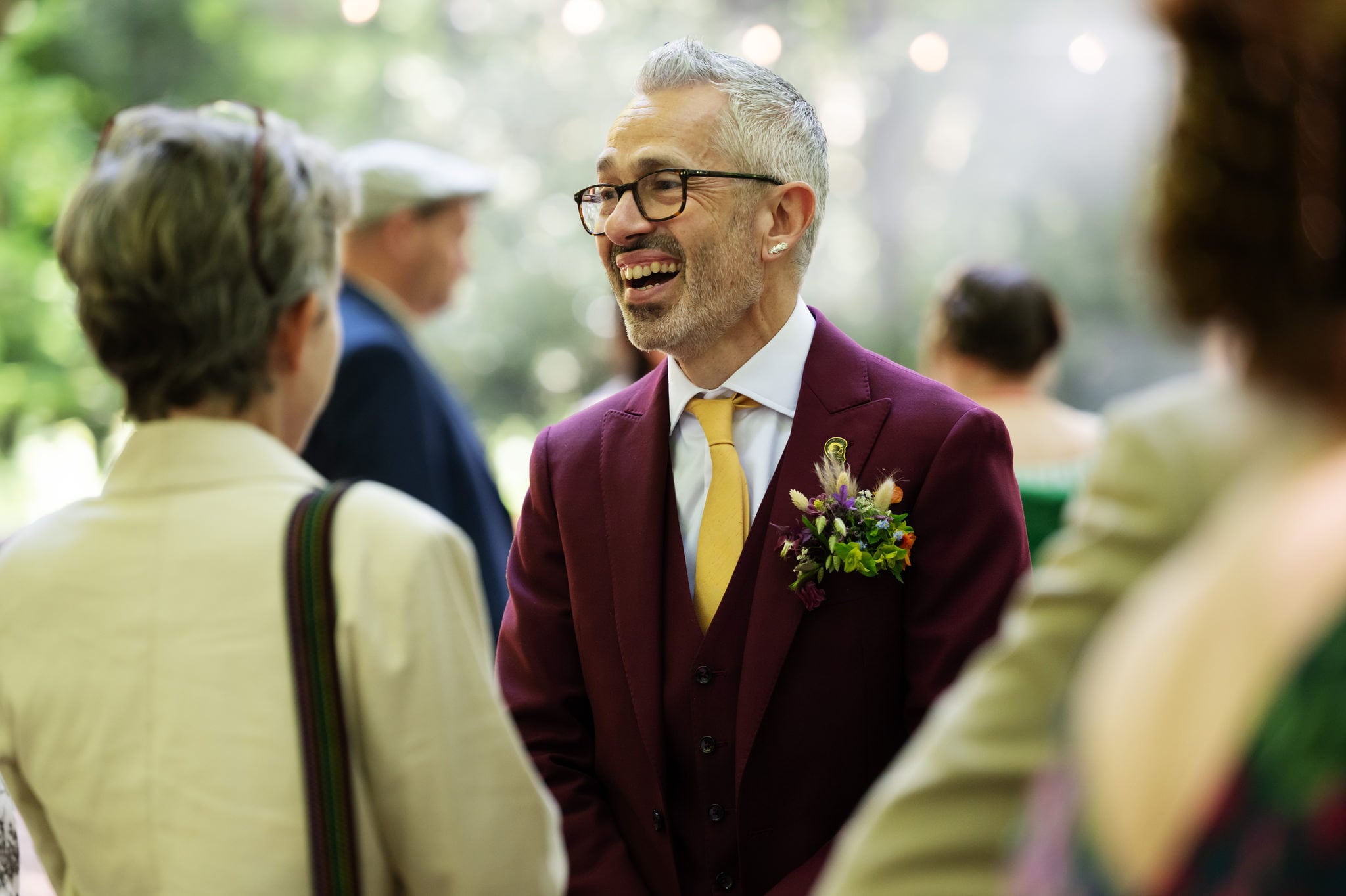 A man in a burgundy suit talking to other people.