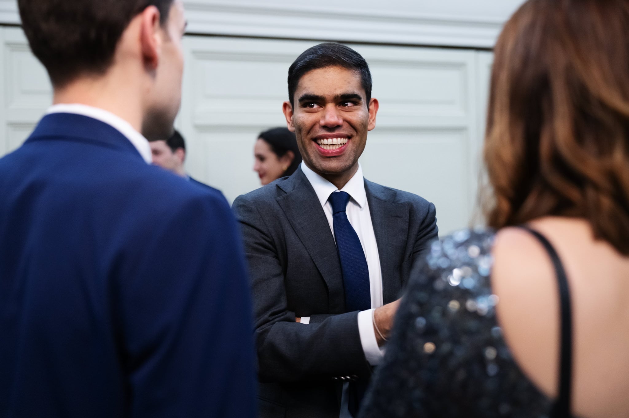 A man in a suit smiles and talks with two other people at an Addington Palace wedding event in Surrey.