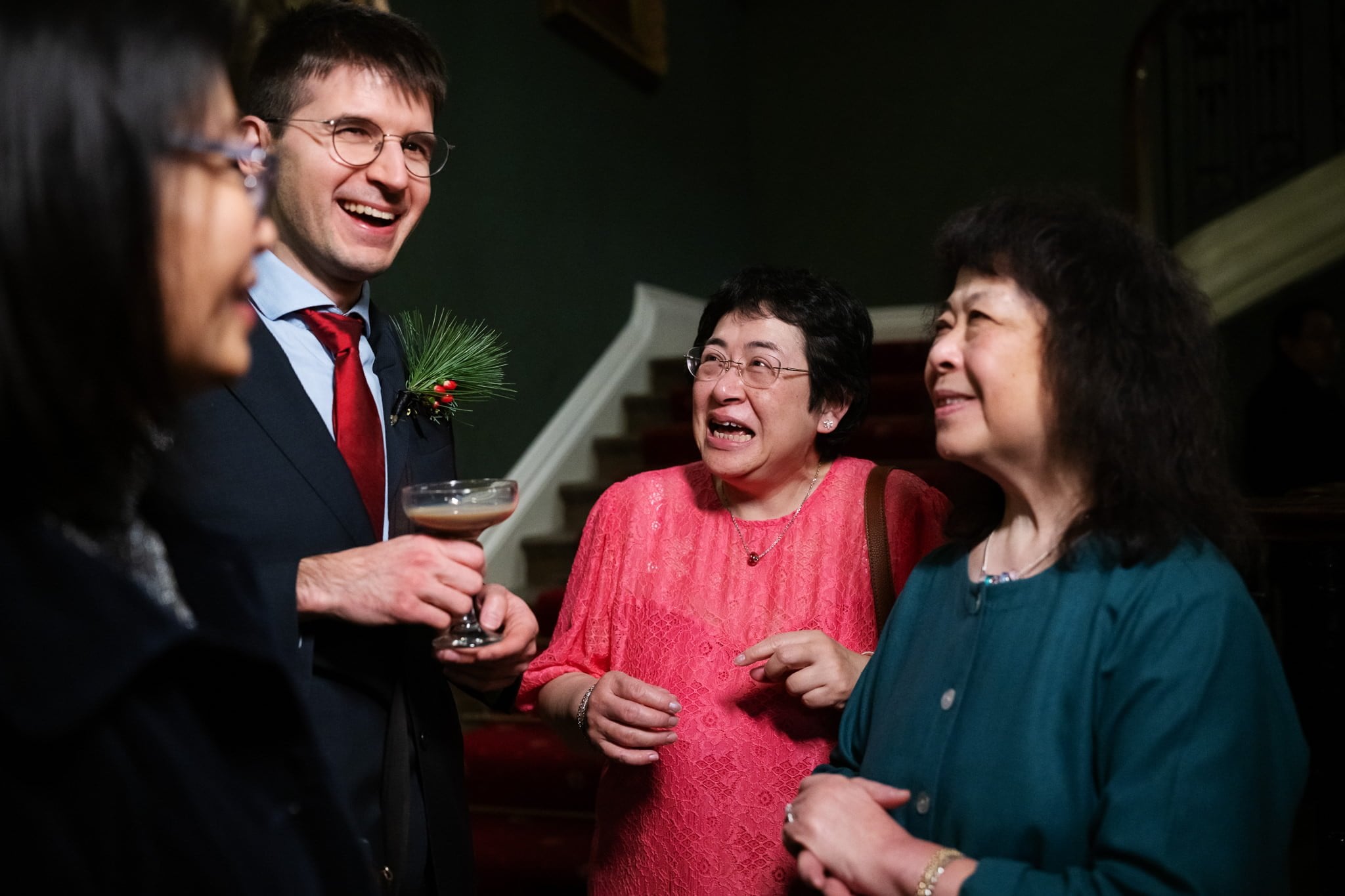 A group of four people, three women and one man, are standing and conversing indoors at an Addington Palace wedding. The man is holding a cocktail, and they appear to be smiling and enjoying the conversation. The ambiance is perfectly captured by the Addington Palace wedding photographer.
