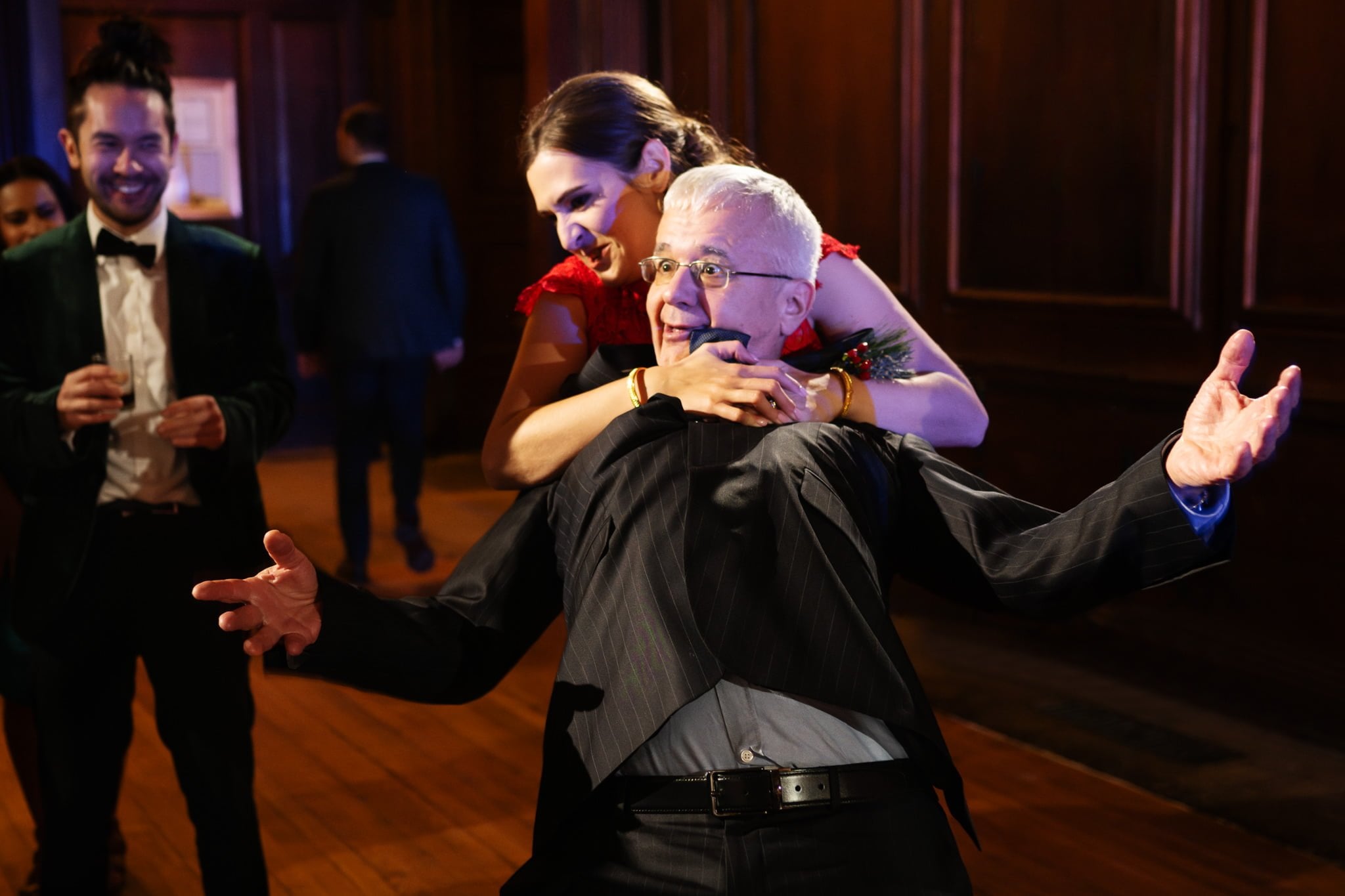 At an elegant Surrey event, a woman playfully hugs an elderly man from behind, while two men in suits stand in the background, capturing the joyous essence of Addington Palace wedding photography.