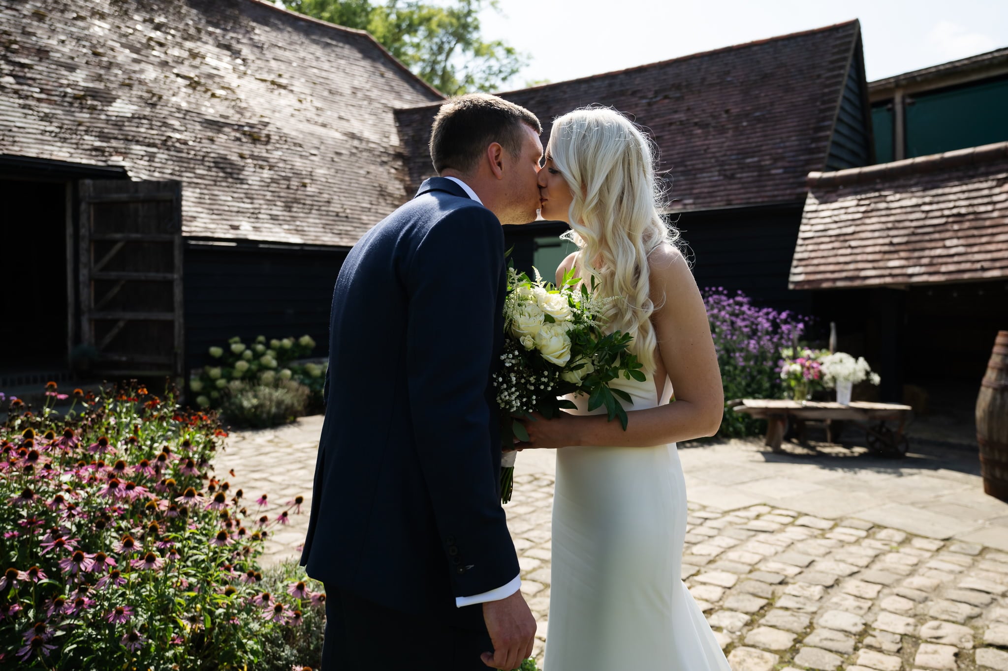 A bride and groom kissing in front of a barn.