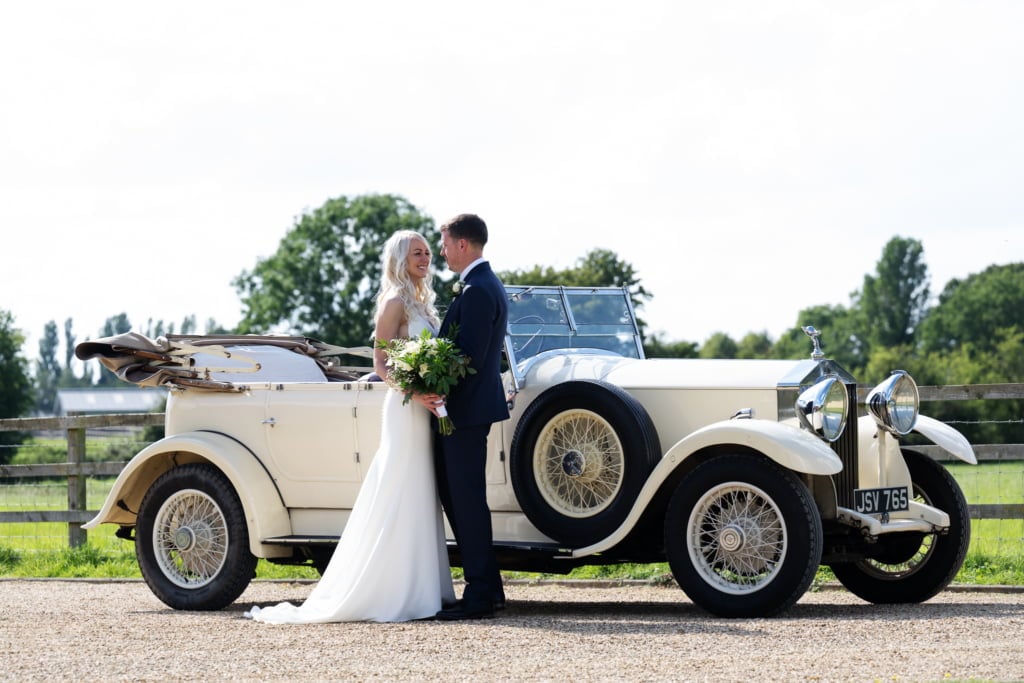 Portrait of bride and groom in front of their wedding car at Bigstrup Farm