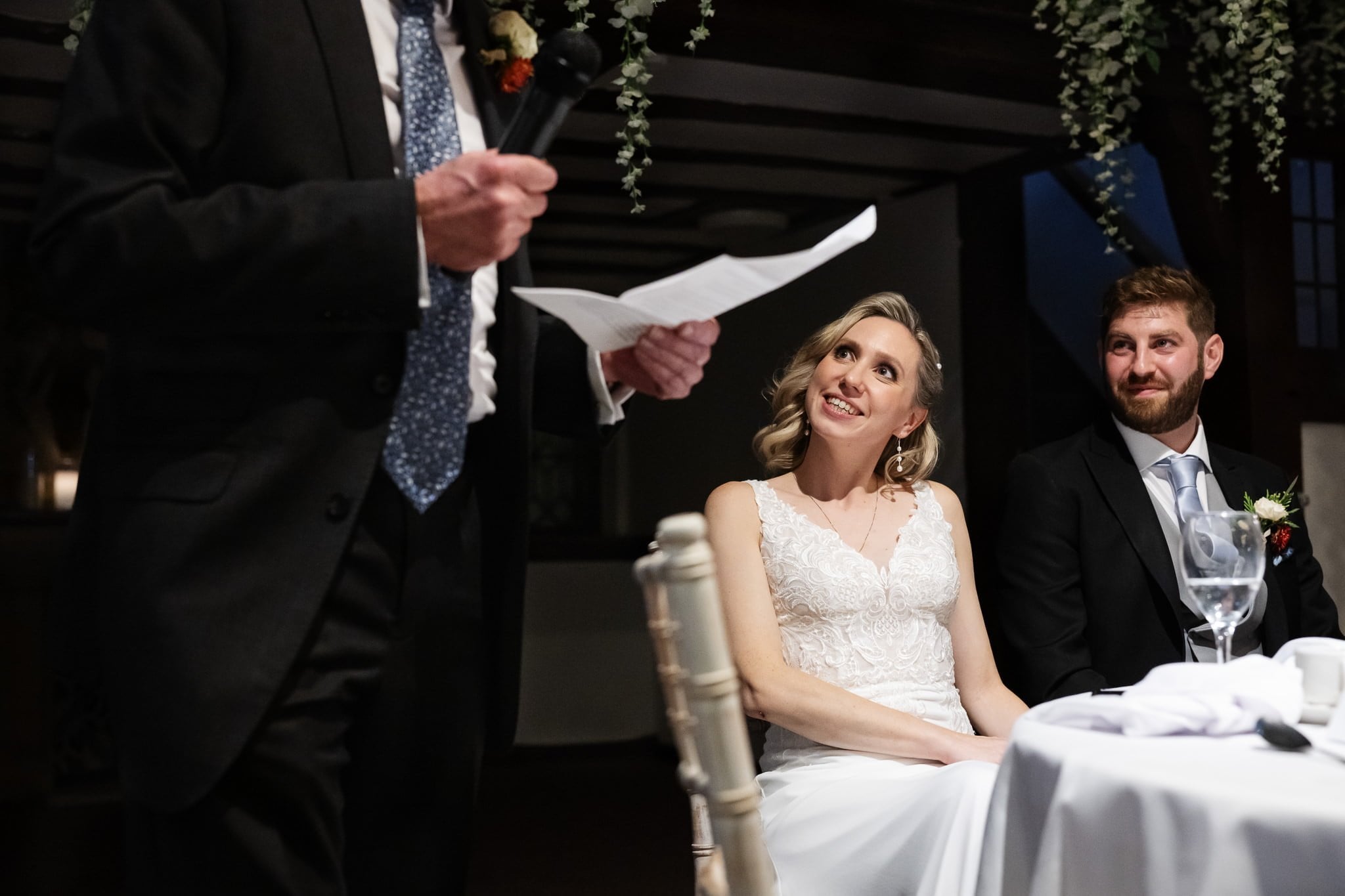 A bride and groom listening to a speech at a wedding reception.