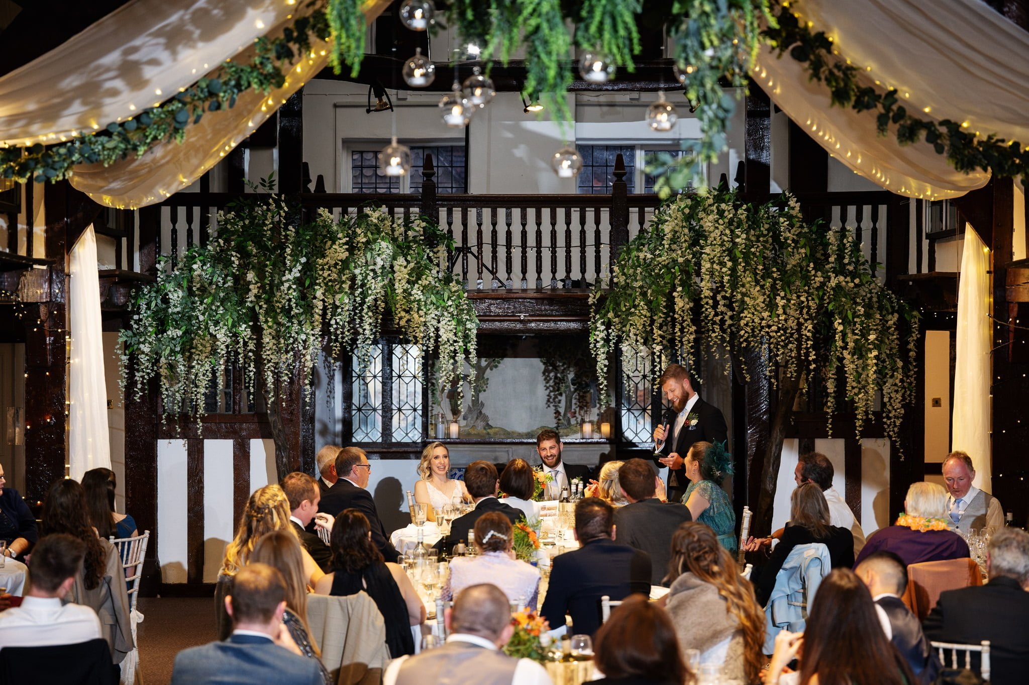 A wedding reception in a large hall with people sitting at tables.