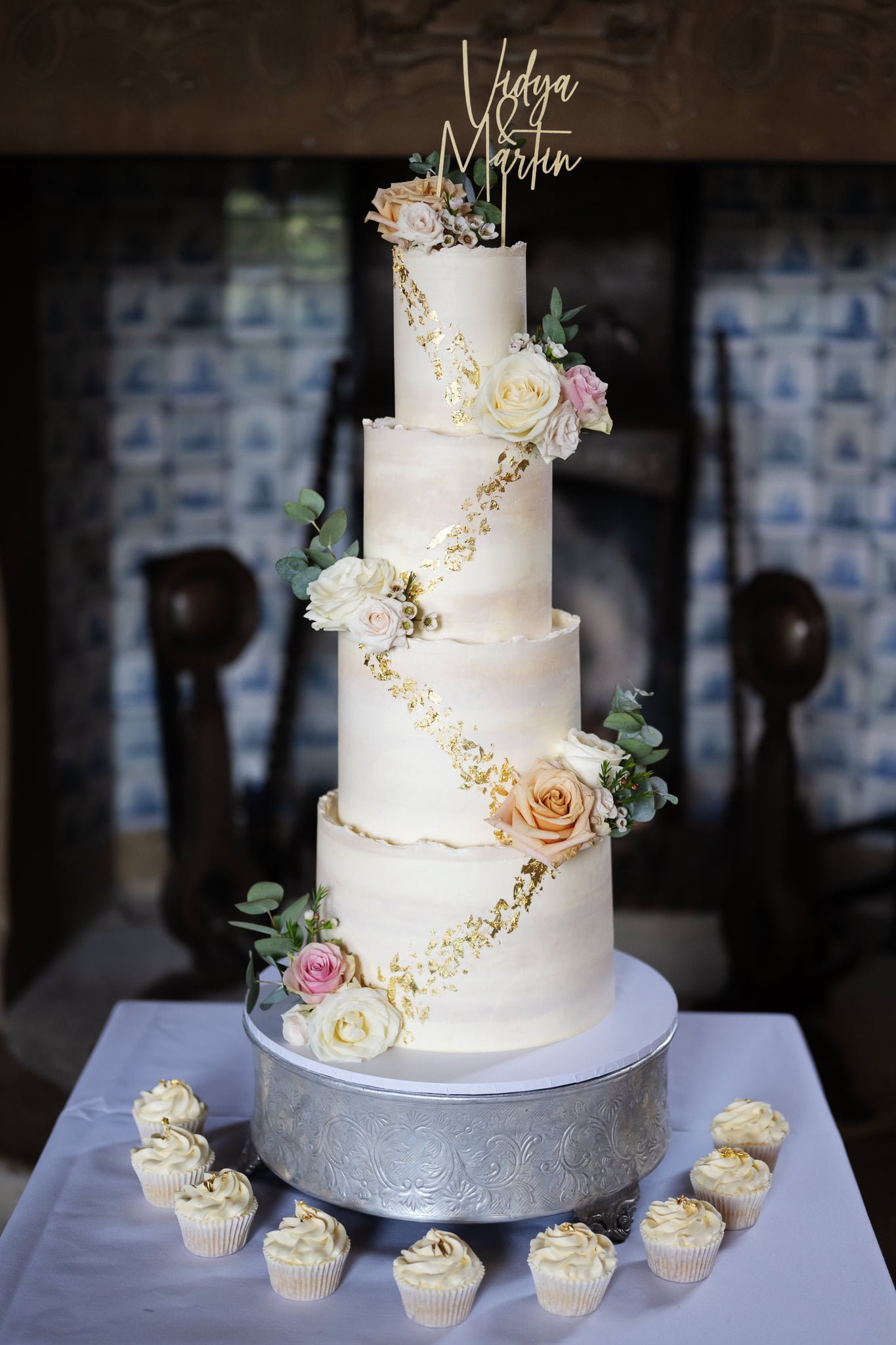 A wedding cake with flowers and cupcakes on a table.