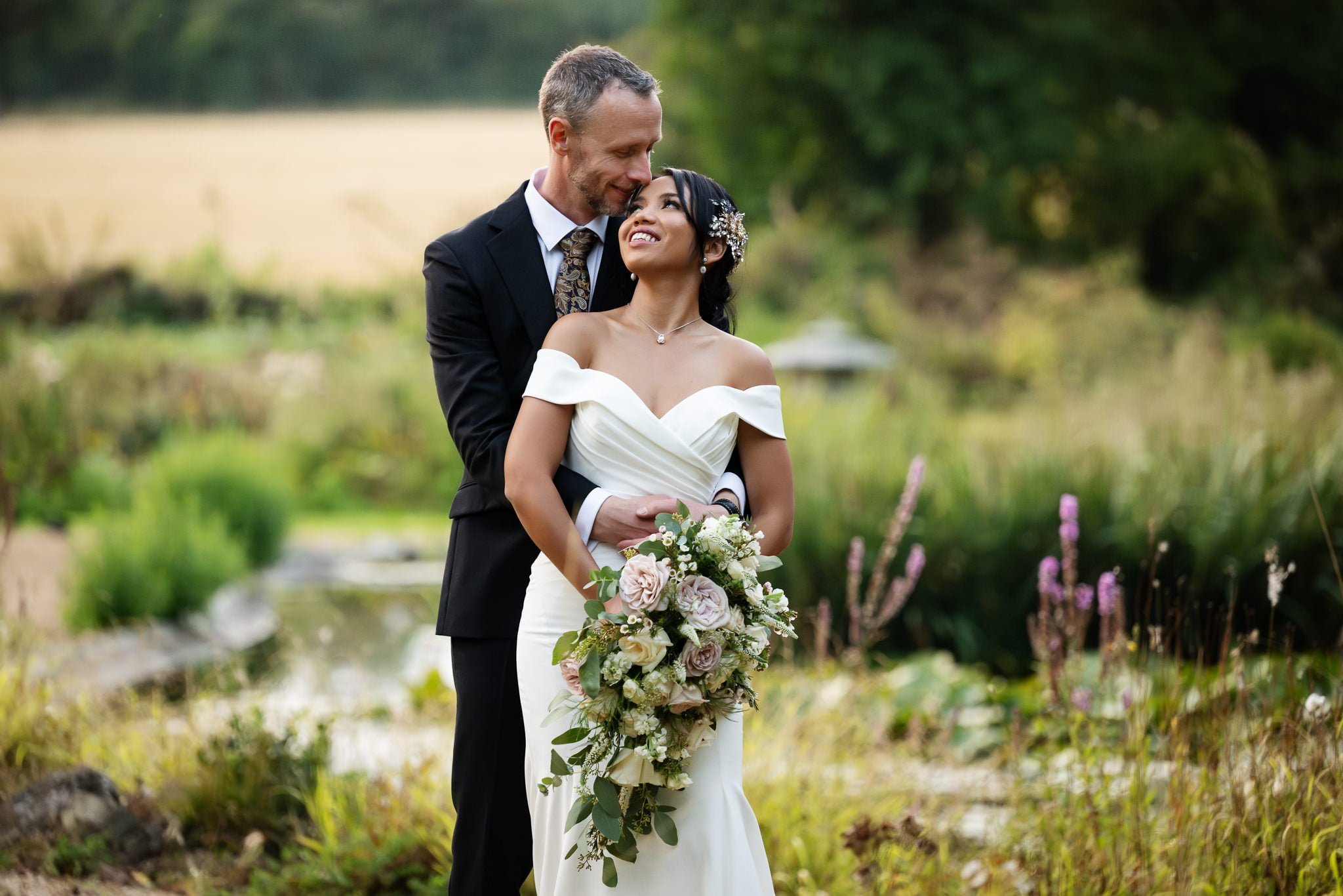 A bride and groom embracing in a field.