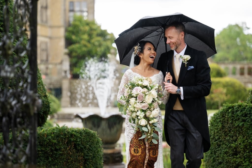 A bride and groom holding an umbrella in front of a castle.