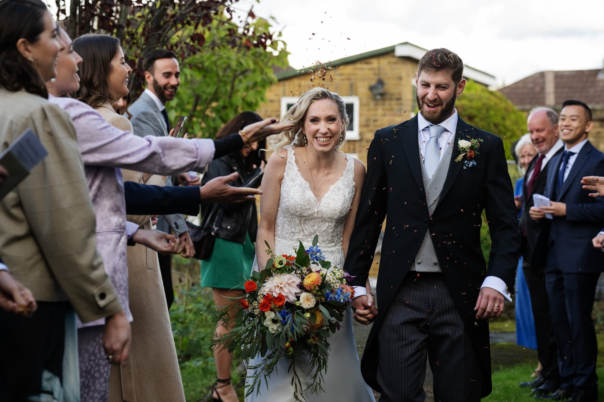A bride and groom walk through a garden with confetti thrown at them.