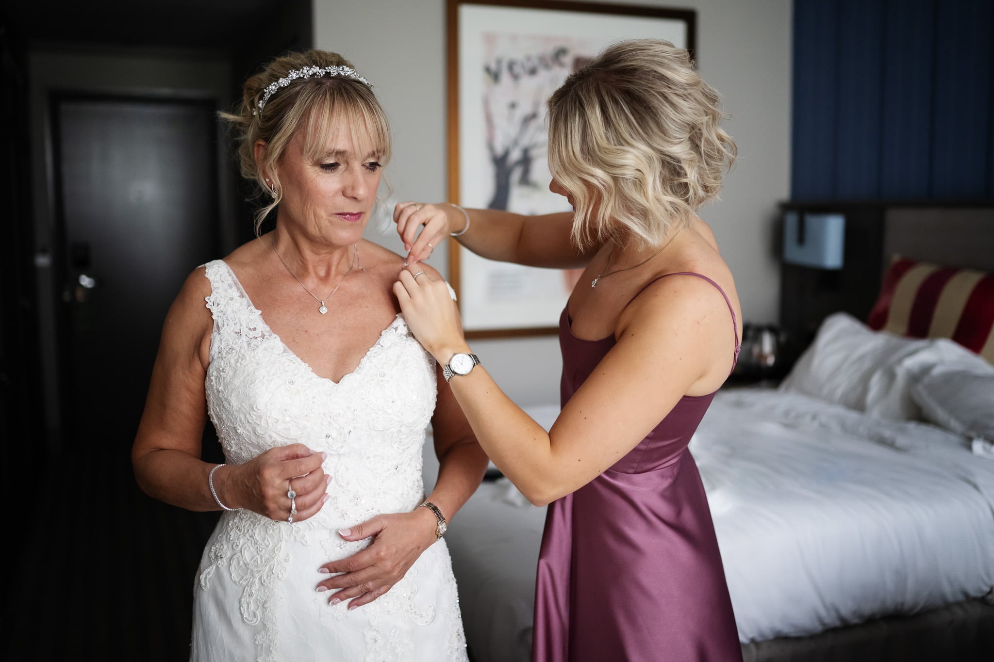 A bride helping her mother put on her wedding dress.