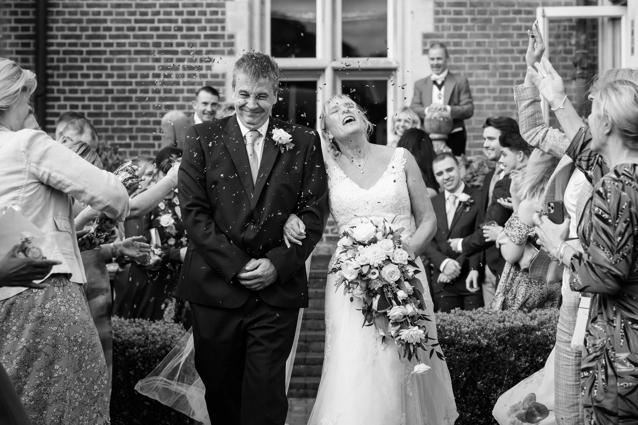 A black and white photo of a bride and groom throwing confetti.