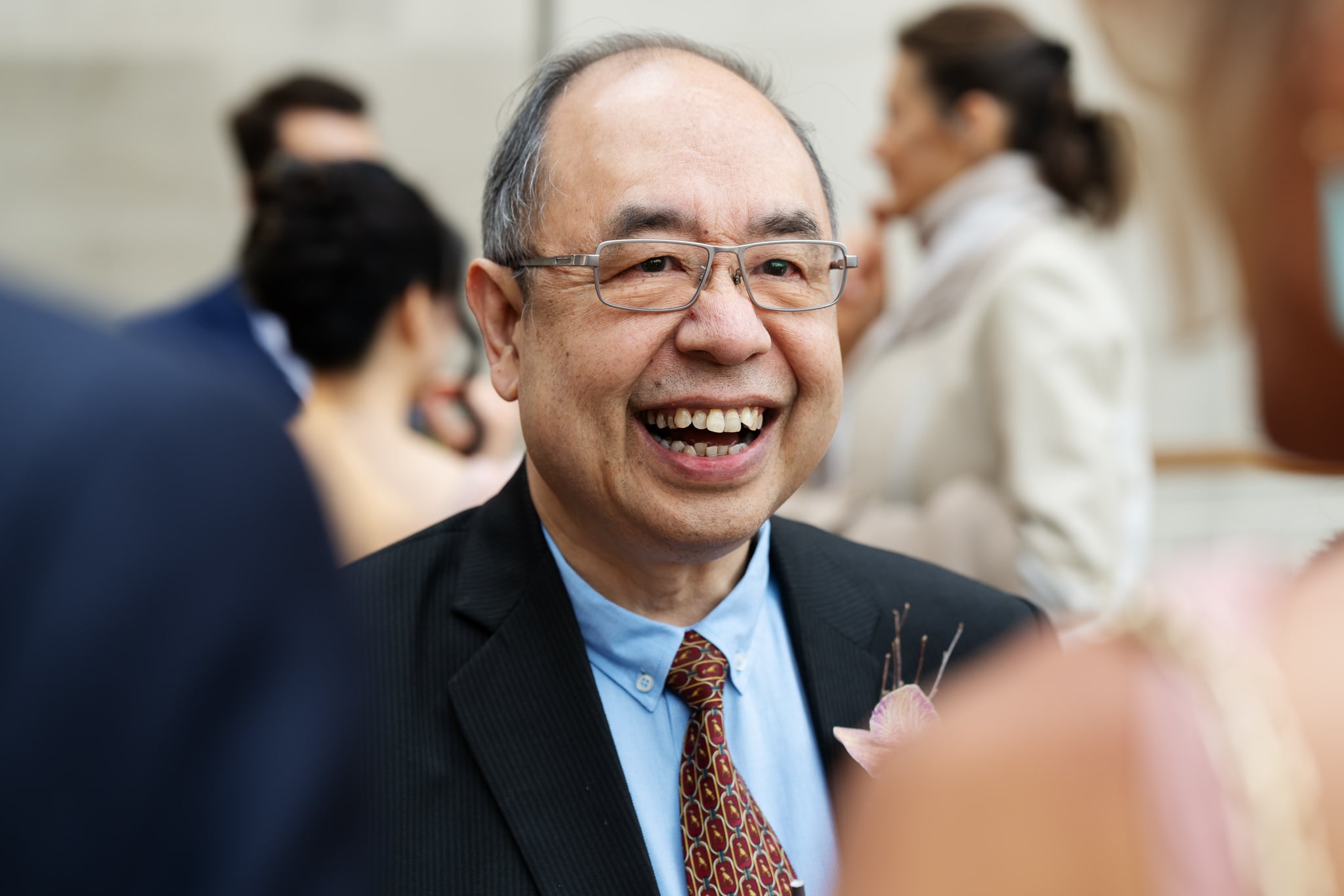 An older man in a suit and tie smiles at an event at No. 4 Hamilton Place, with people conversing in the background—a charming scene perfect for a London wedding.