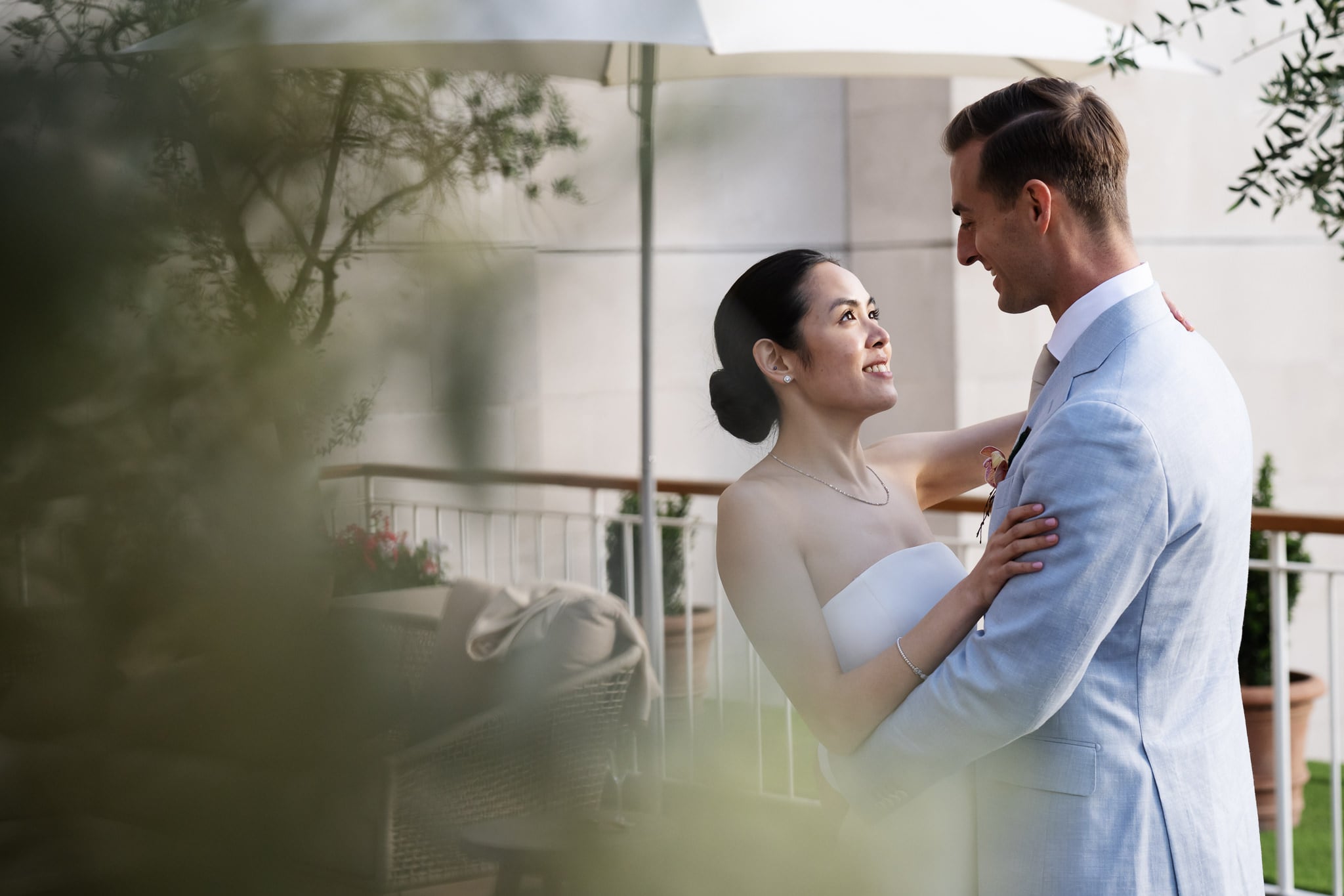 A bride and groom embrace outdoors at No. 4 Hamilton Place, looking at each other and smiling, with greenery and patio furniture in the background during their London wedding.