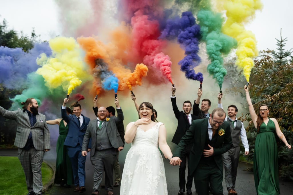 Bride and groom walking with bridal party behind them using colourful smoke bombs at Rivervale Barn wedding