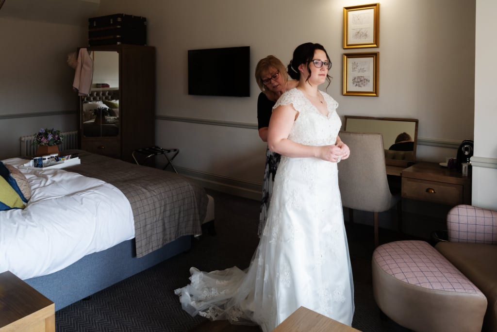 The bride is helped into her wedding dress in the ready for her wedding at De Vere Latimer Estate