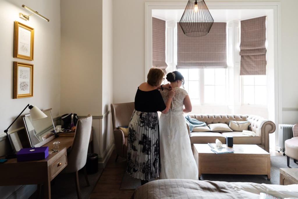 The bride's mother is helping the bride into her wedding dress in the ready for her wedding at De Vere Latimer Estate