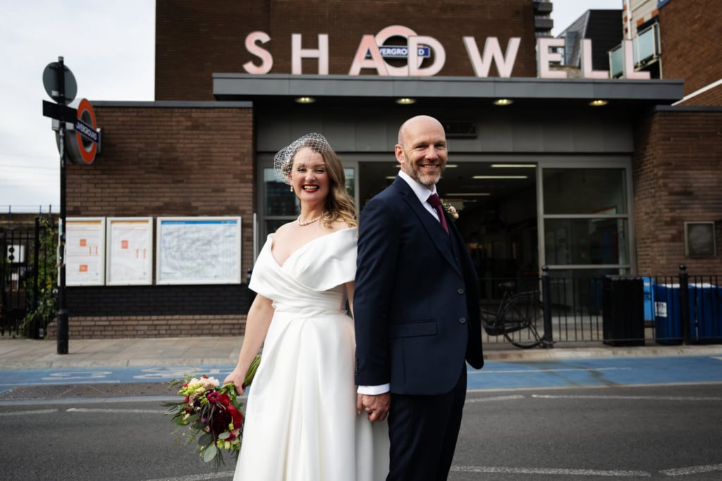 A portrait of bride and groom in front of Shadwell underground station in London