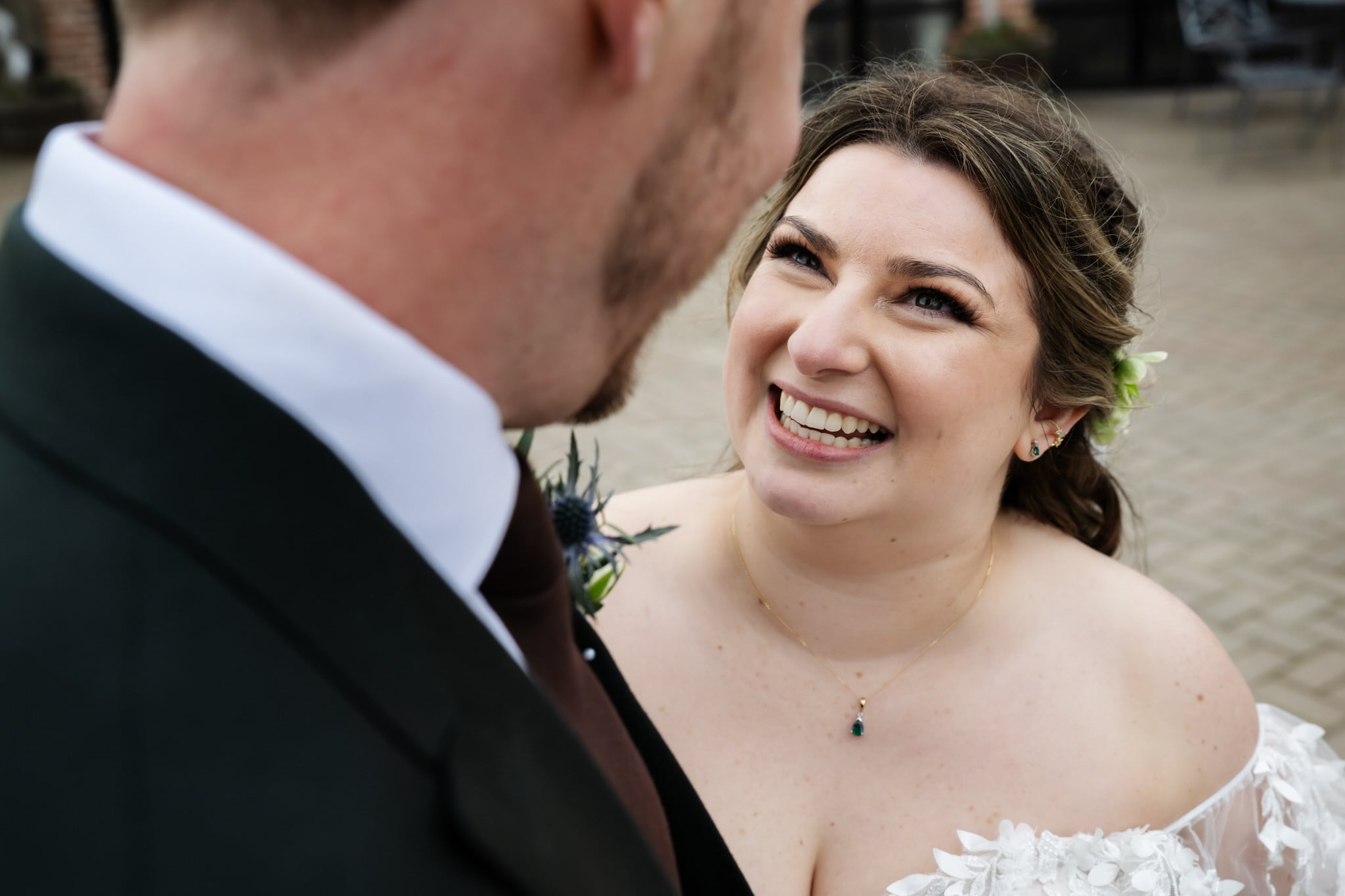 A bride in a white dress smiles and looks up at the groom in a suit and tie outdoors on a paved surface at Stratton Court Barn.